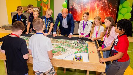 Wethouder Anko Goudswaard kijkt met kinderen naar LEGO League tafel.
