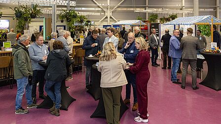 Groep mensen staan rondom tafels met elkaar in gesprek op informatiemarkt in World Horticenter.