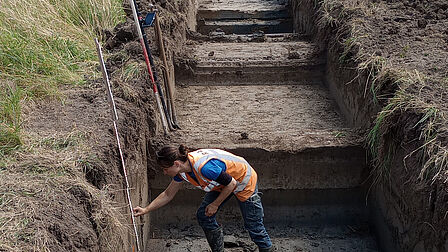 Foto man doet onderzoek in een proefsleuf. 