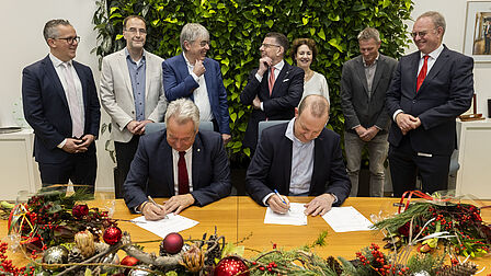 Groep mensen achter tafel waarbij wethouder van der Stee en David van Mechelen, Chief Financial Officer van Royal FloraHolland overeenkomsten ondertekenen.